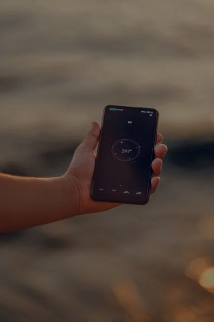 Hand holding smartphone displaying digital wallet app interface, blurred monitor in background.